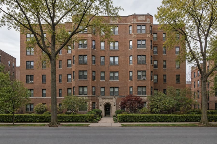 A pre-war brick garden apartment building with an arched entrance and a planted forecourt