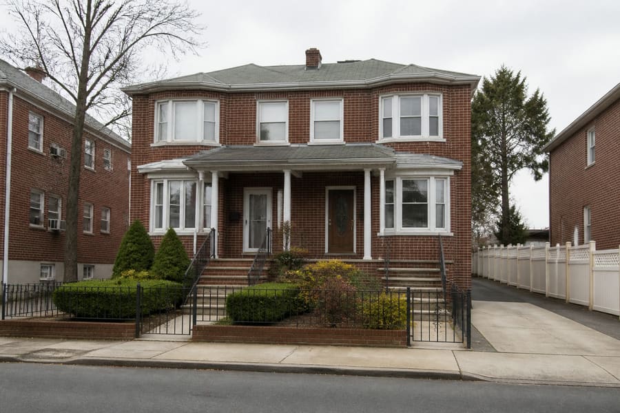 A semi-detached two-storey brick house with steps up to a covered porch and a small front yard