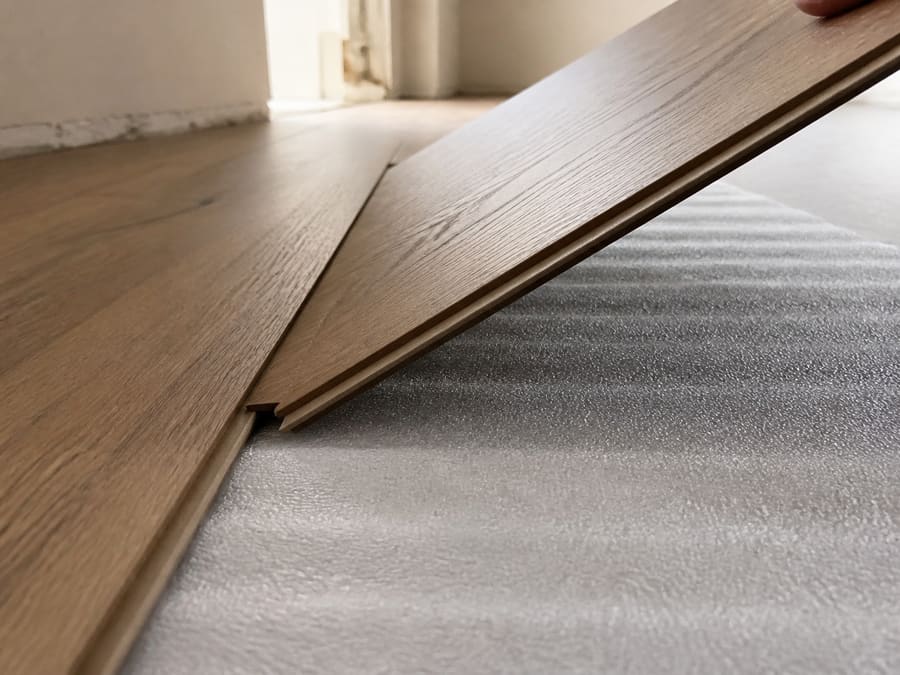 A laminate plank being angled down into the click joint of the previous row over foam underlayment