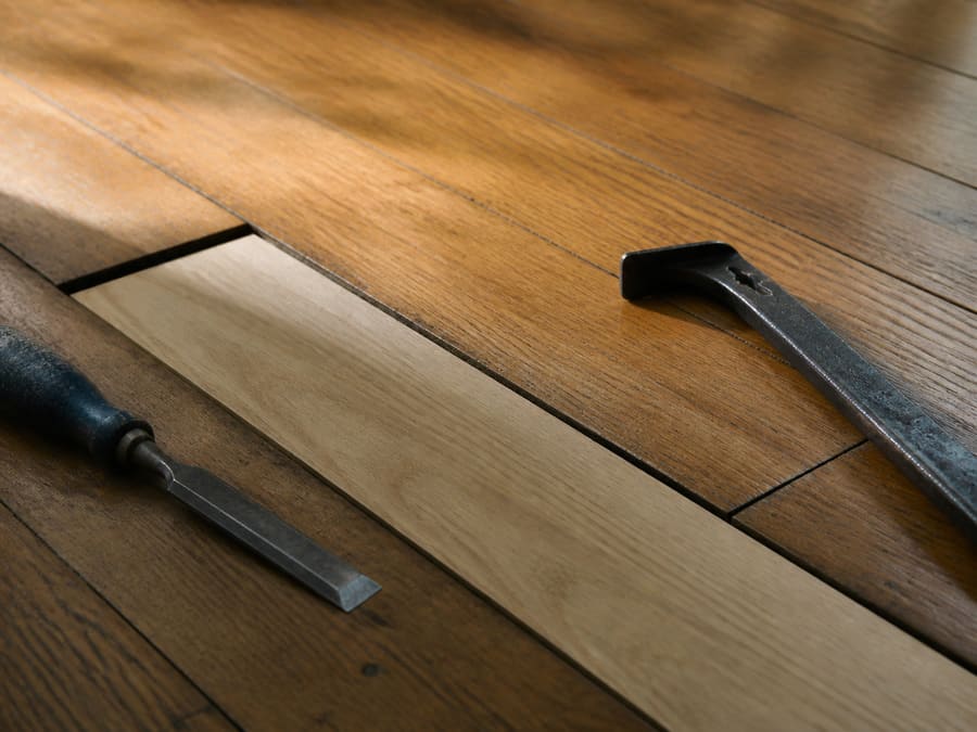 A replacement board being fitted into a gap in an existing oak floor, the new wood visibly lighter